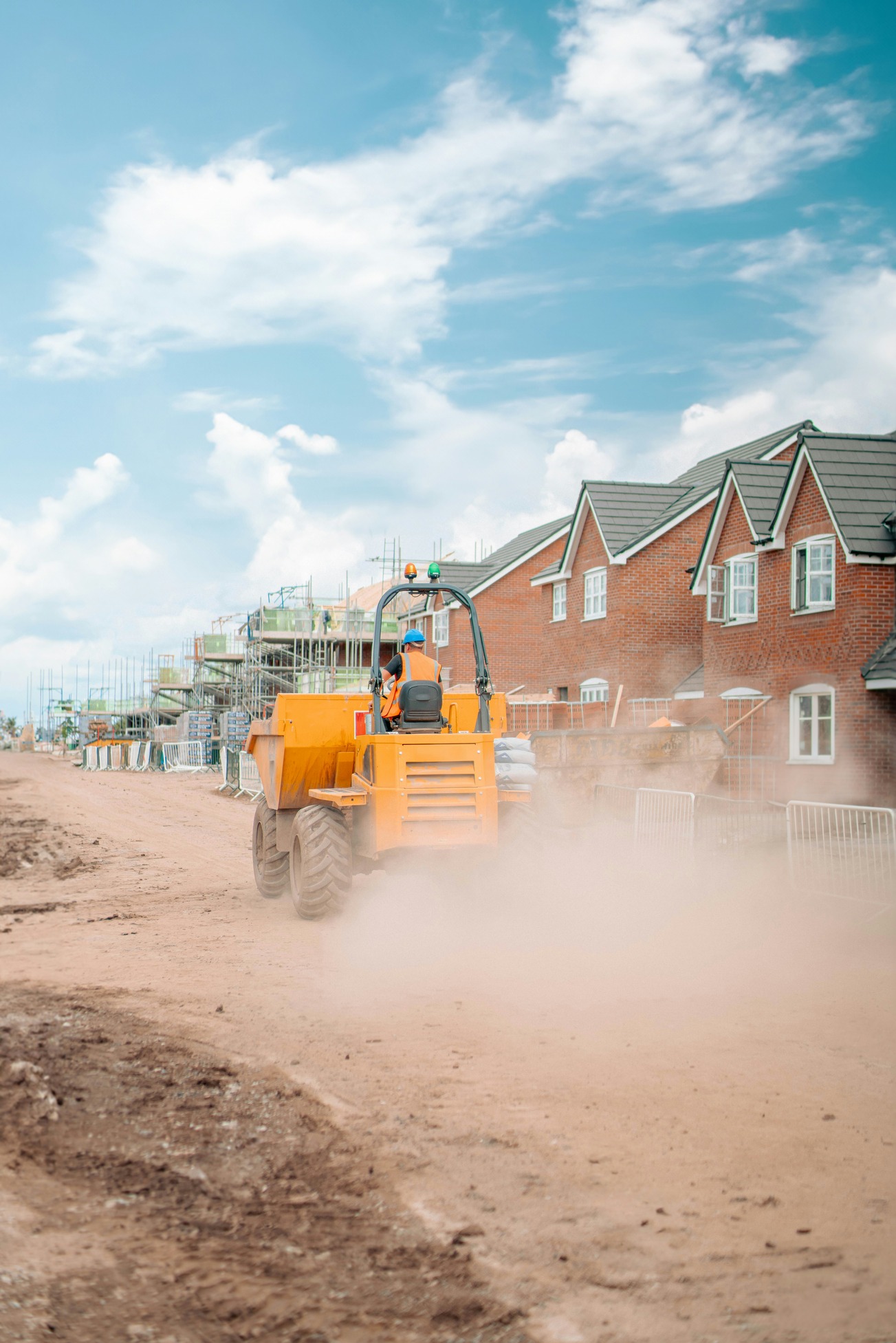 Heavy plant driving along dirt road by new houses